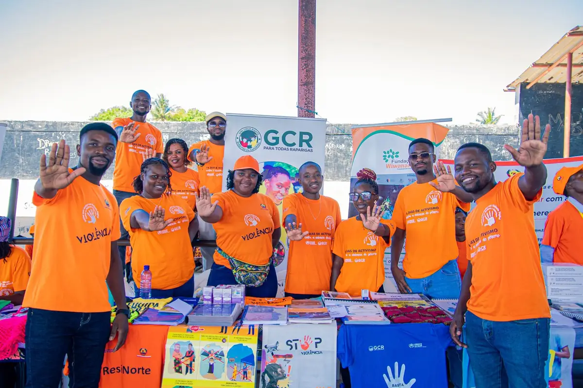 Activistas e equipa da GCR, de camisolas cor-de-laranja, fazem o gesto de «basta» com a mão junto a uma banca da campanha
