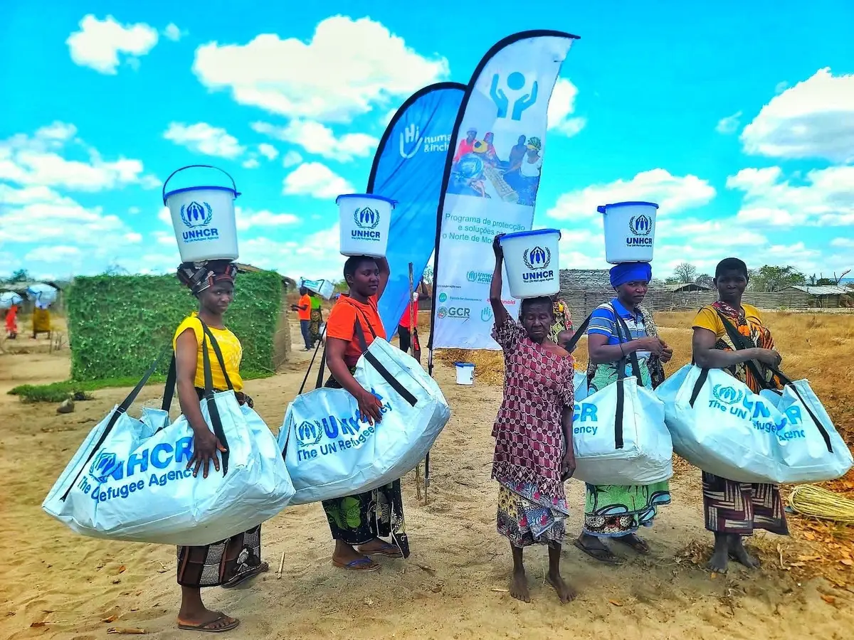 Mulheres transportam kits de artigos não alimentares e baldes durante a distribuição em Nonge, Macomia