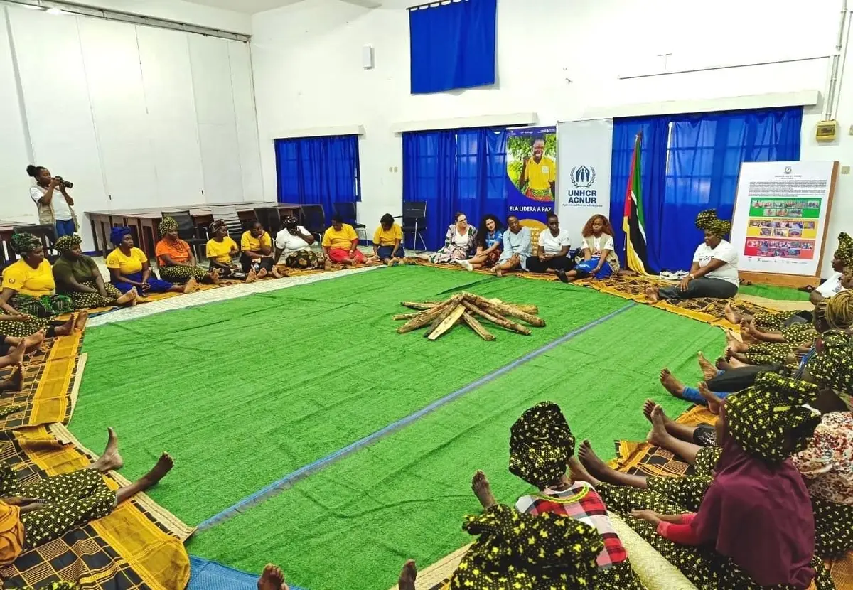 Mulheres sentadas em círculo à volta de uma fogueira simbólica, vistas de costas, num espaço seguro da GCR em Pemba