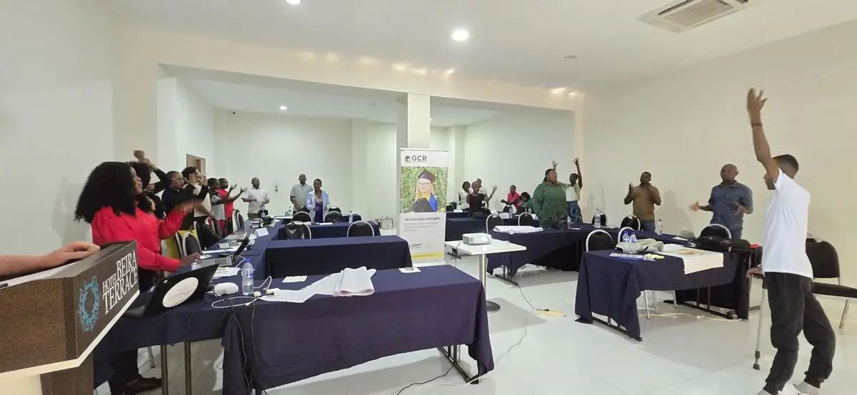 Participantes de pé, de braços erguidos, durante uma dinâmica na formação sobre espaços seguros inclusivos na Beira